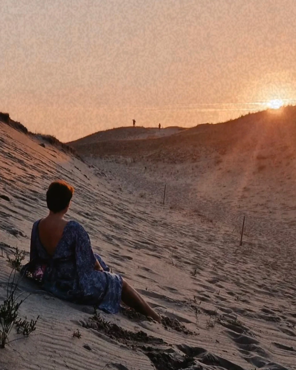 Aleksandra Drūteikaitė sėdi ant smėlio kopų ir žiūri į saulėlydį